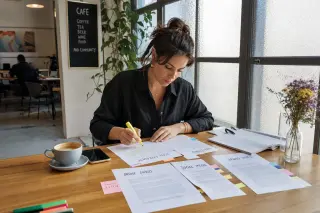 Freelance communication specialist concentrating on niche-defining notes at a sunlit café table, thoughtful and authentic workspace
